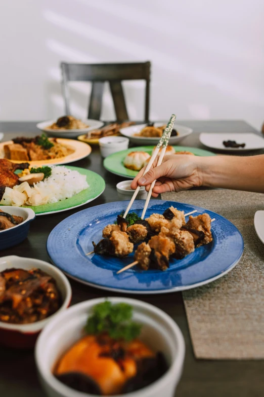 a group of people sitting at a table with plates of food, chopsticks, malaysian, hand on table, at home