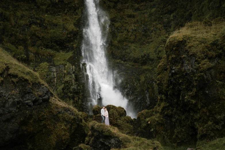 a man standing in front of a waterfall, by Hallsteinn Sigurðsson, pexels contest winner, hurufiyya, nathalie emmanuel, with subtitles, wide high angle view, lena oxton