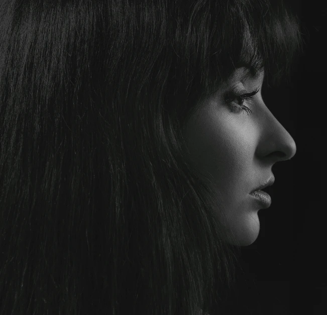 a black and white photo of a woman with long hair, photorealism, profile image, black bangs, soft lighting and focus, portrait of mournful