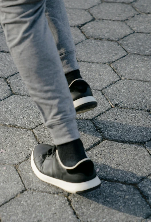 a person riding a skateboard down a cobblestone street, grey pants and black dress shoes, zoomed in, wearing white sneakers, worn pants