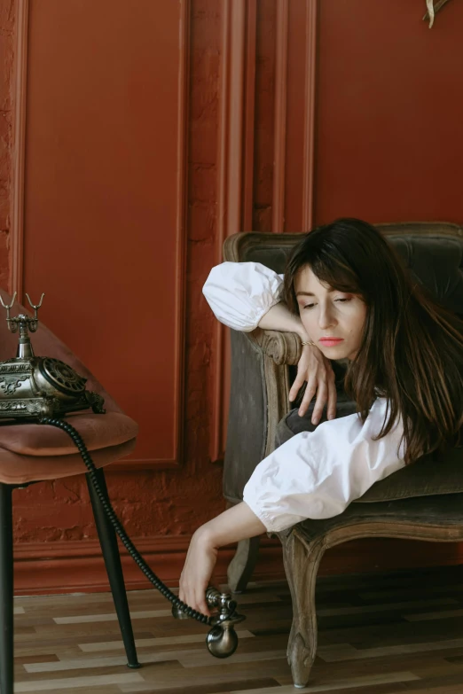 a woman sitting on top of a couch next to a table, inspired by Wilhelm Hammershøi, pexels contest winner, baroque, sleepy fashion model face, girl with dark brown hair, sitting in a chair, promotional image