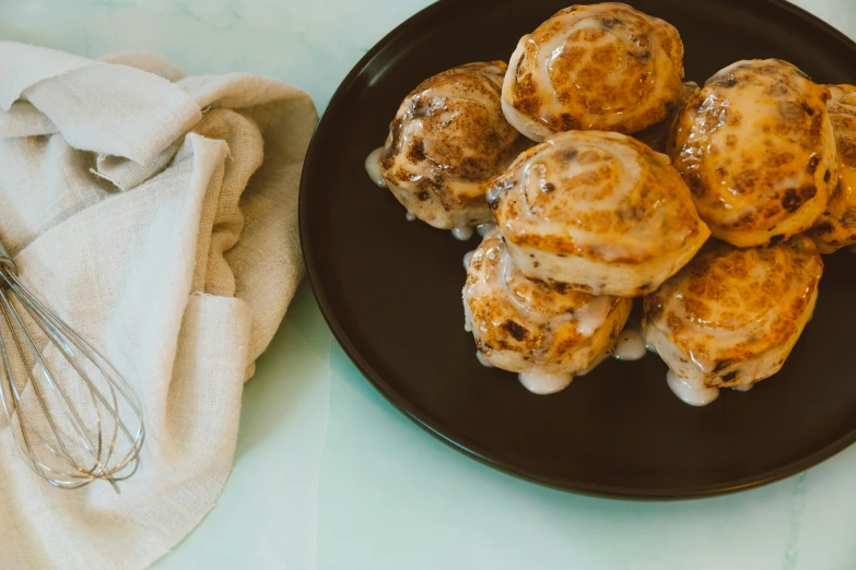 a black plate topped with cinnamon buns next to a whisk, unsplash, dumplings on a plate, 6 pack, background image, pastel'