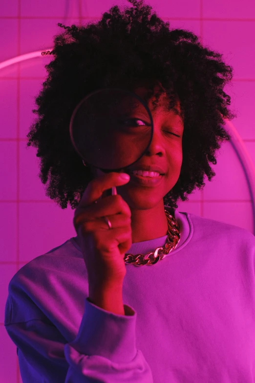 a woman holding a magnifying glass in front of her face, an album cover, trending on pexels, afrofuturism, brightly lit purple room, admiring her own reflection, 2 1 savage, looking happy