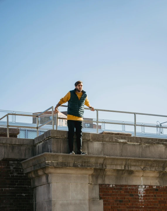 a man standing on top of a brick building, wearing a yellow hoodie, bridge, lachlan bailey, observation deck
