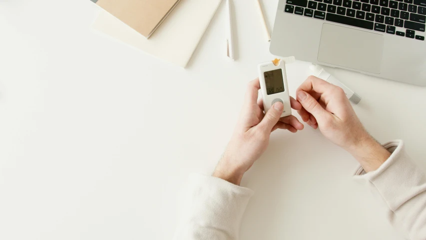 a person holding a cell phone next to a laptop, holding a syringe, on a white table, 9 9 designs, watch photo