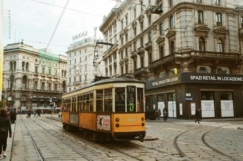 a yellow trolley traveling down a street next to tall buildings, a colorized photo, by Emma Andijewska, pexels contest winner, renaissance, milan jozing, 🦩🪐🐞👩🏻🦳, square, brown