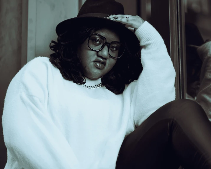 a black and white photo of a woman wearing a hat, an album cover, inspired by Ion Andreescu, pexels contest winner, nerdy black girl super hero, wearing a white sweater, plus-sized, casual pose