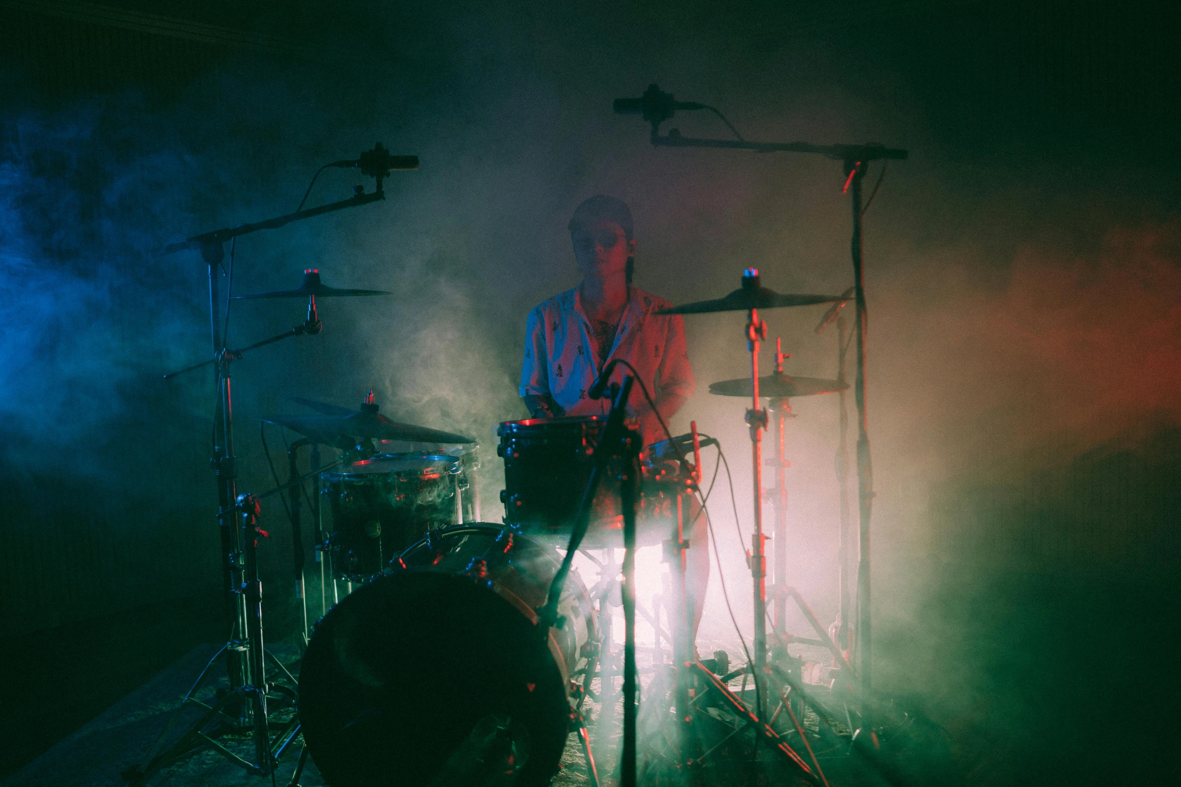 a man that is sitting in front of a drum, an album cover, unsplash, ( ( stage lights ) ), bleached, 15081959 21121991 01012000 4k, muted neon smoke