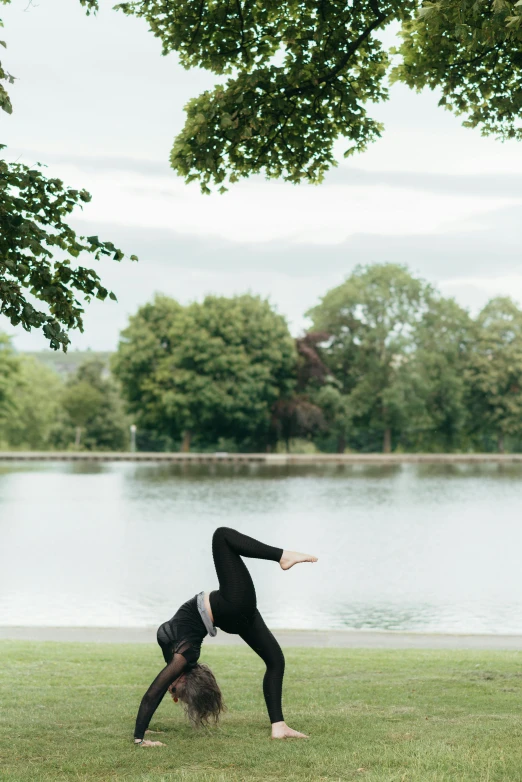 a woman doing a handstand in front of a lake, by Rachel Reckitt, arabesque, in the park, with a sleek spoiler, dwell, england