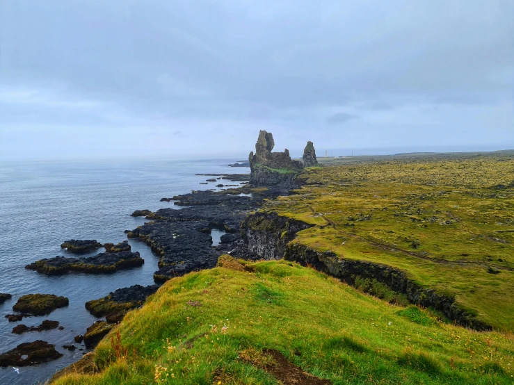 a large body of water sitting on top of a lush green hillside, inspired by Þórarinn B. Þorláksson, pexels contest winner, black domes and spires, rocky seashore, conde nast traveler photo, lava in the background