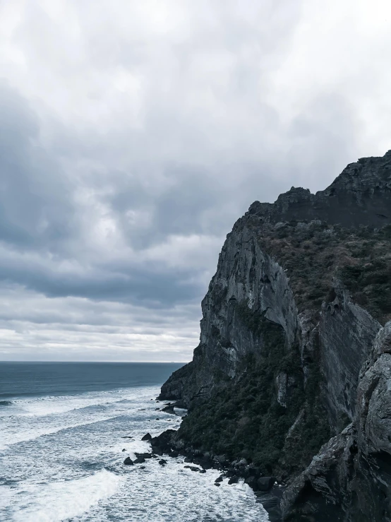 a man standing on top of a cliff next to the ocean, inspired by Kōshirō Onchi, unsplash contest winner, mingei, overcast gray skies, today\'s featured photograph 4k, devils horns, texture