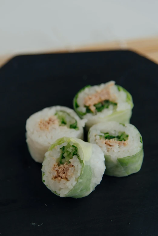 a black plate topped with sushi rolls on top of a wooden table, green: 0.5, daopao, cucumber, canopee