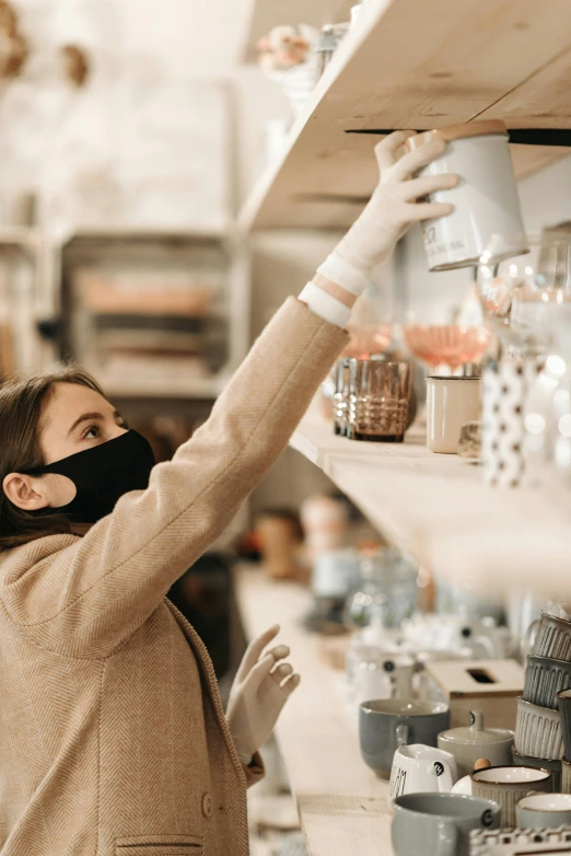 a woman wearing a face mask in a store, trending on pexels, renaissance, holding a candle holder, busy, shelf, wearing gloves