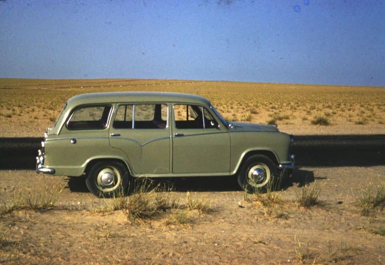 an old car is parked on the side of the road, by Bertram Brooker, olive green, in the desert beside the gulf, slide show, square