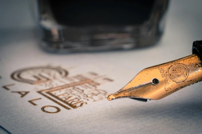 a fountain pen sitting on top of a piece of paper, pexels contest winner, private press, intricate gold linework, thumbnail, flowing lettering, opening shot