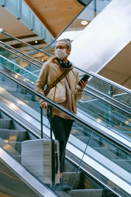 a woman standing on an escalator looking at her cell phone, face mask, in suitcase, square, thumbnail