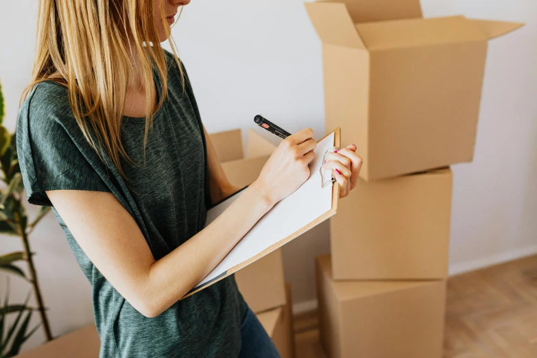 a woman writing on a clipboard in front of boxes, a sketch, pexels contest winner, lachlan bailey, moving, prop, simple form