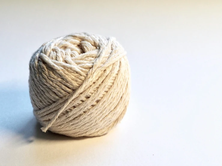 a ball of yarn sitting on top of a table, beige cream natural muted tones, white background and fill, thumbnail, 33mm photo