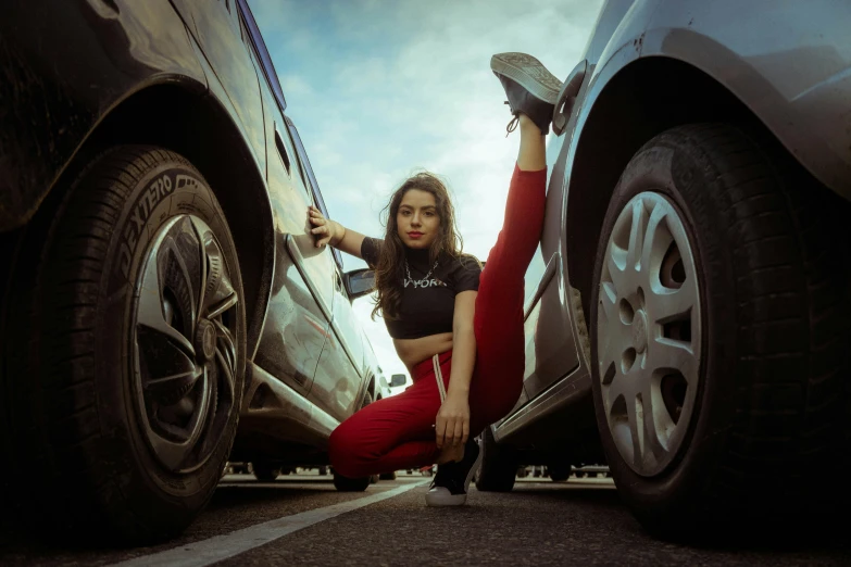 a woman sitting on the ground next to a parked car, pexels contest winner, acrobatic pose, black and red, avatar image, wearing a track suit