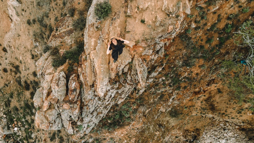 a man standing on top of a mountain next to a cliff, a photo, aerial view top down, avatar image, female ascending, black and terracotta