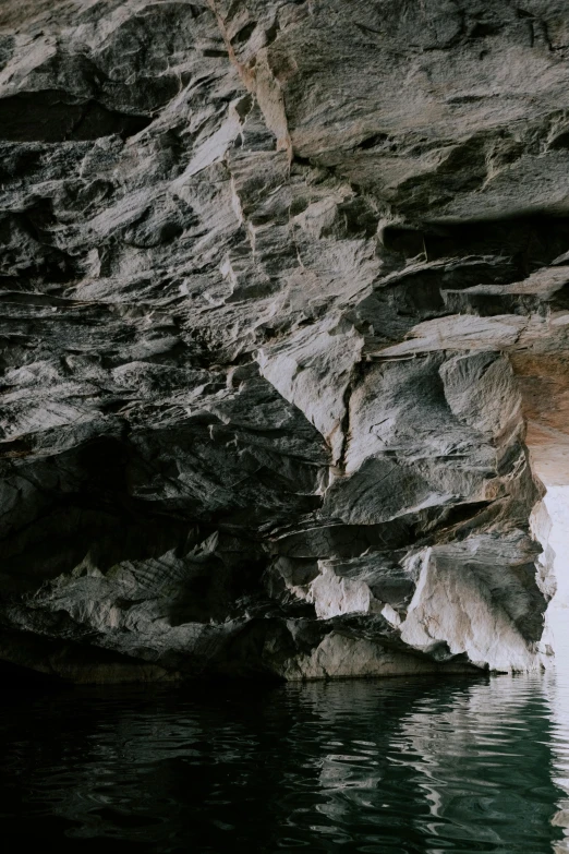 a man standing on top of a rock next to a body of water, a cave painting, by Elsa Bleda, panoramic, grey, sandstone, thirst