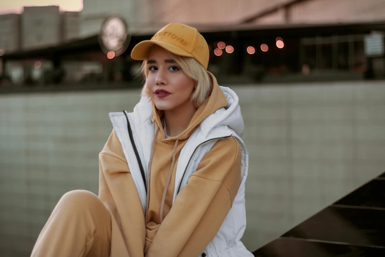 a woman sitting on a bench wearing a hat, trending on pexels, wearing a yellow hoodie, gradient white to gold, wearing a tracksuit, promotional image