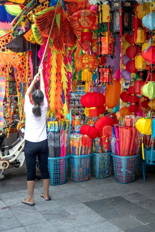 a woman that is standing in front of a store, inspired by Cui Bai, happening, colorful paper lanterns, split near the left, straw, red flags holiday