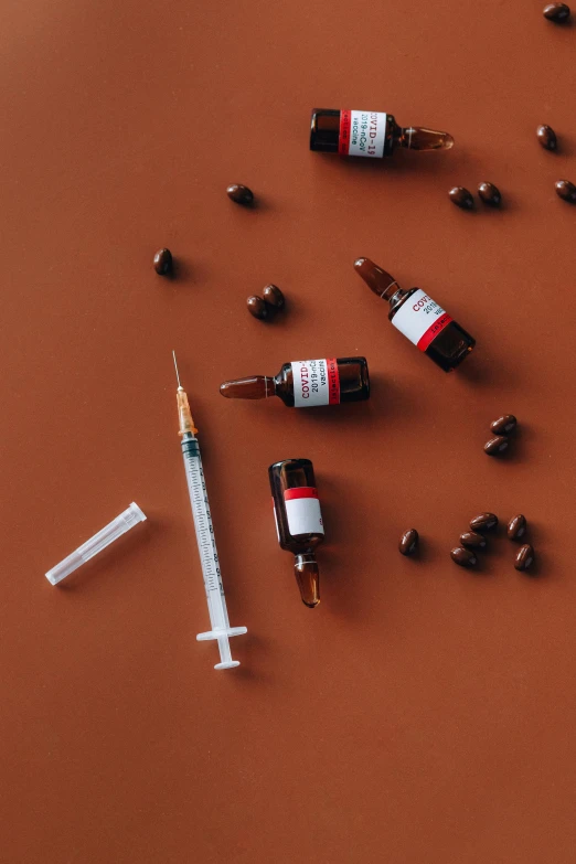 a bottle of medicine and a syll on a brown surface, a still life, by Julia Pishtar, trending on pexels, syringe, red and black color scheme, knolling, brown