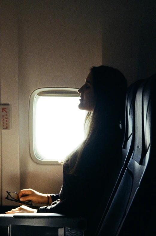 a woman sitting in an airplane looking out the window, sun behind her, a woman's profile, leaving a room, bad light