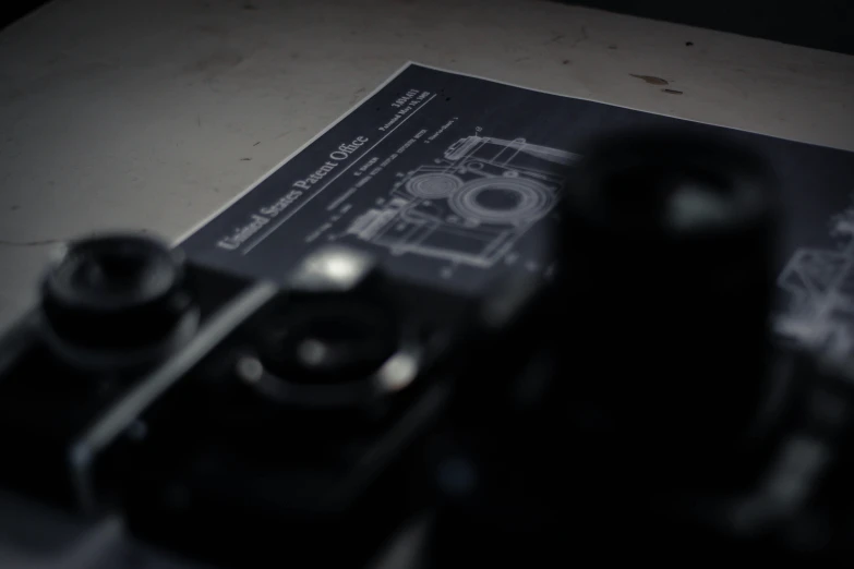a camera sitting on top of a table next to a book, an etching, by Adam Marczyński, industrial design blueprint, matte black paper, cinematic poster, front shot