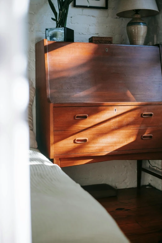 a wooden desk sitting in a bedroom next to a bed, by Jan Tengnagel, unsplash, light and space, old experimentation cabinet, directional sunlight skewed shot, late 1 9 6 0's, drop shadow
