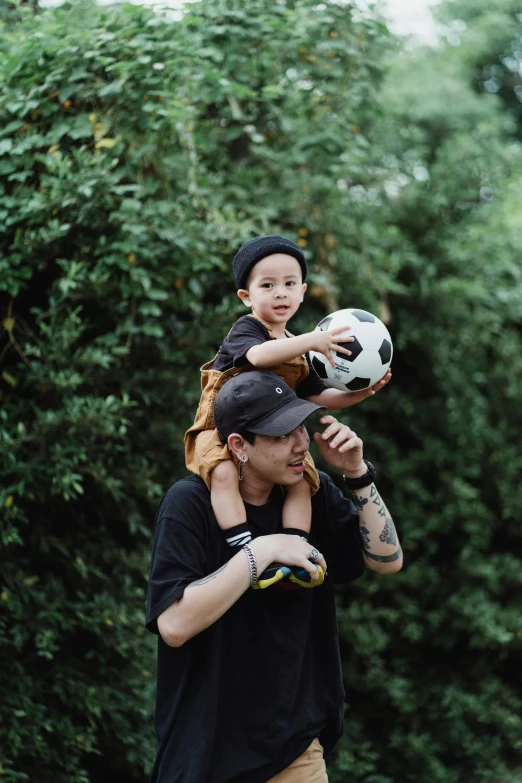 a man carrying a child on his shoulders, by Basuki Abdullah, pexels contest winner, realism, soccer ball, with black beanie on head, in garden, edgar maxence and ross tran