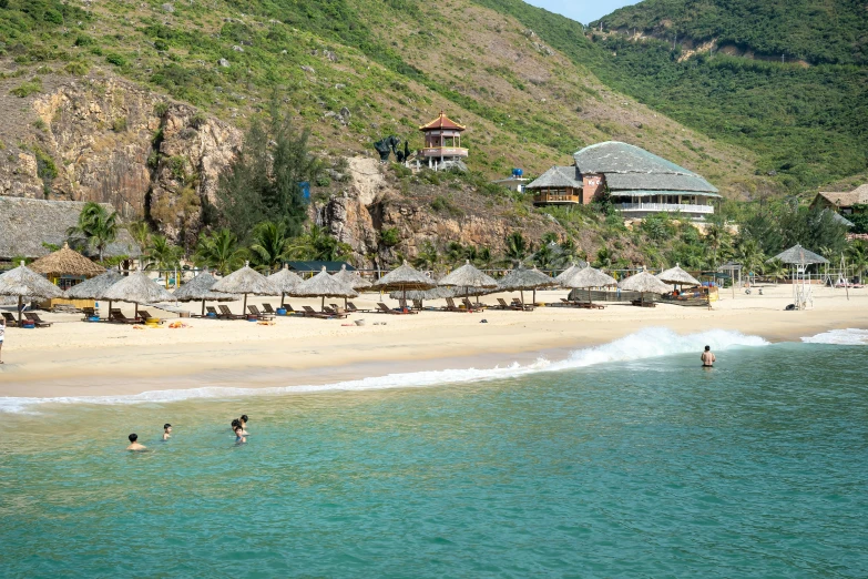 a group of people standing on top of a sandy beach, vietnam, luxurious onsens, parasols, viewed from the ocean