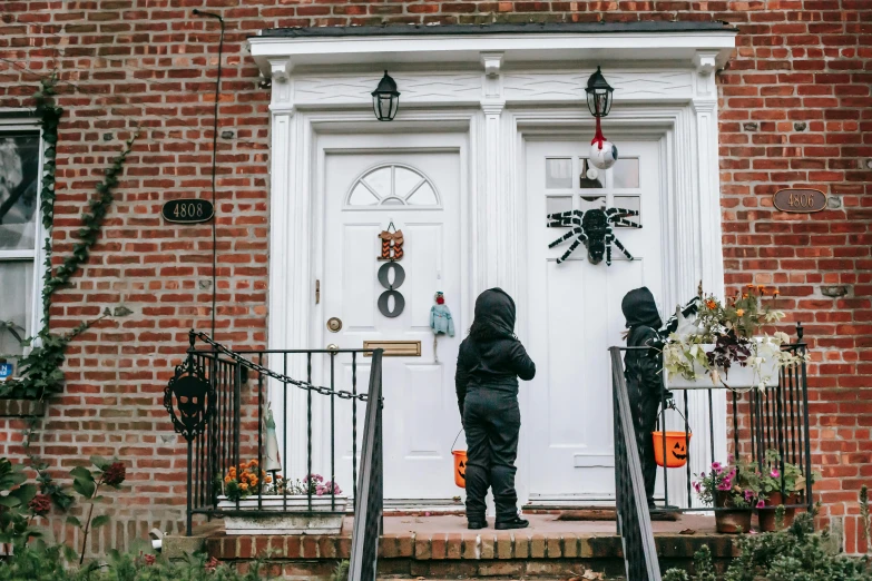 a little boy that is standing in front of a door, halloween decorations, people walking down a street, 😭🤮 💔, outdoor photo