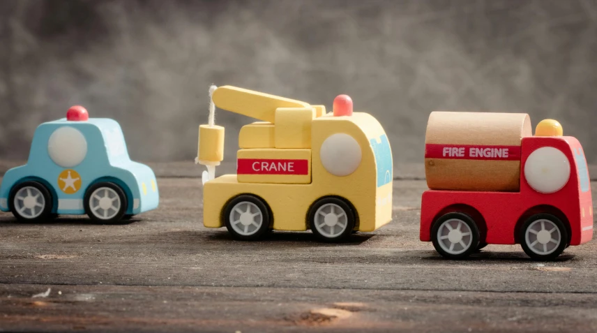 a group of toy cars sitting on top of a wooden table, on grey background, playing with a small firetruck, product shot, multicoloured