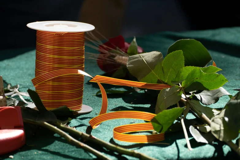 a spool of thread and a spool of flowers on a table, inspired by Bruce Munro, unsplash, process art, orange ribbons, hoses, exterior shot, lianas