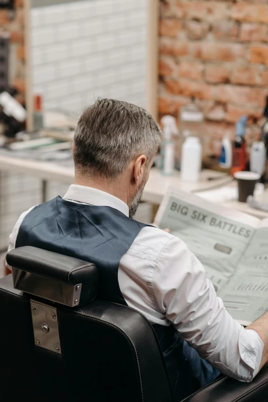 a man sitting in a chair reading a newspaper, a cartoon, trending on pexels, undercut haircut, back - shot, in a workshop, dapper