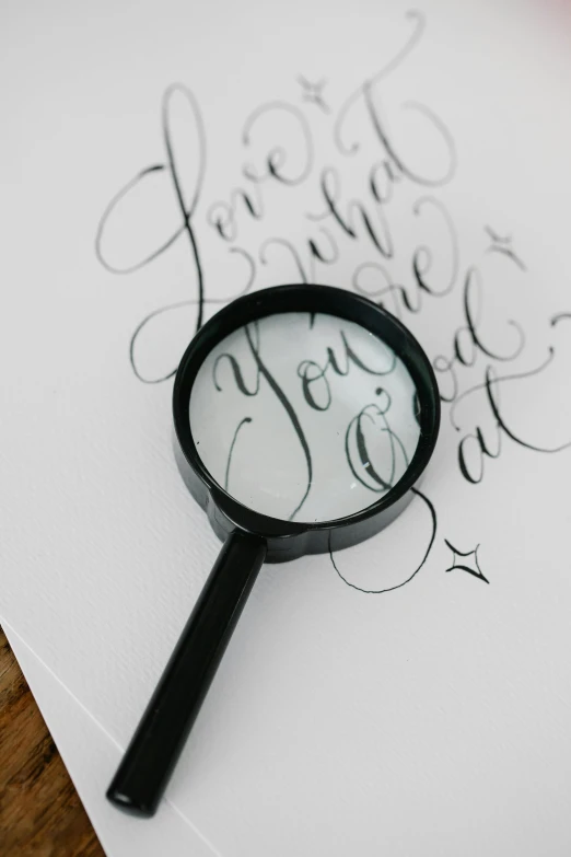 a magnifying glass sitting on top of a piece of paper, by Lucette Barker, letterism, caligraphy, high-quality photo