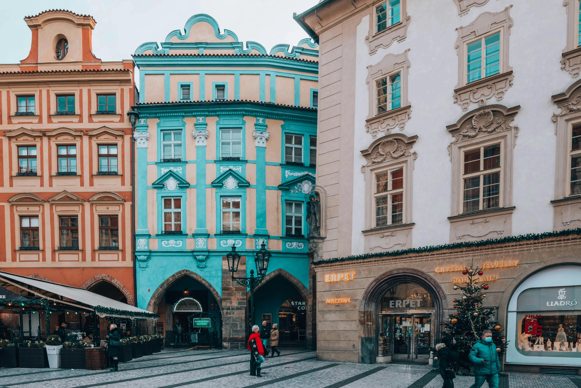 a group of people walking down a street next to tall buildings, by Emma Andijewska, pexels contest winner, art nouveau, pink and teal, prague, square, big arches in the back