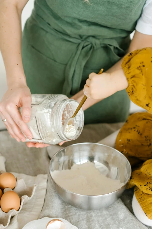 a woman pouring eggs into a bowl on top of a table, a portrait, trending on pexels, flour dust, glass jar, gif, baking cookies