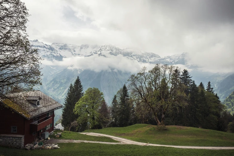 a house sitting on top of a lush green hillside, a picture, inspired by Peter Zumthor, pexels contest winner, les nabis, snow capped mountains, overcast, lauterbrunnen valley, panoramic view