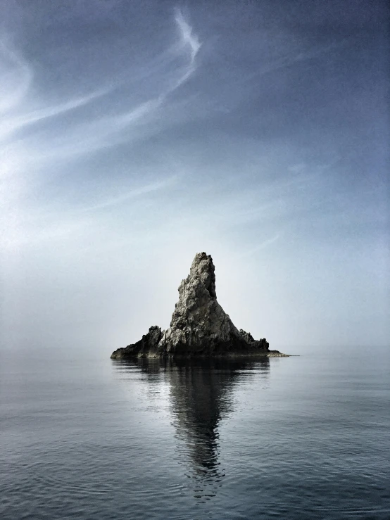 a rock in the middle of a body of water, a picture, inspired by Michal Karcz, unsplash contest winner, capri coast, resembling a crown, pareidolia, looking like a bird