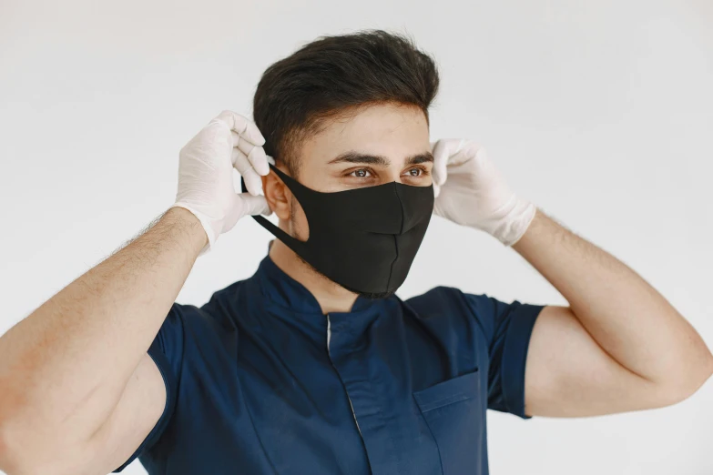 a man in a blue shirt and white gloves adjusts his face mask, trending on pexels, all black matte product, dentist, he is wearing a black, australia