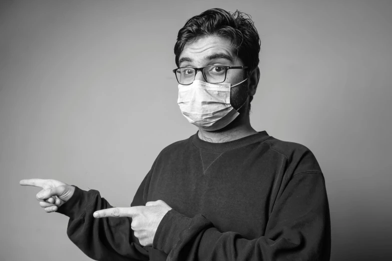 a black and white photo of a man wearing a face mask, a black and white photo, pexels, serial art, with pointing finger, nerd, nursing, asian man