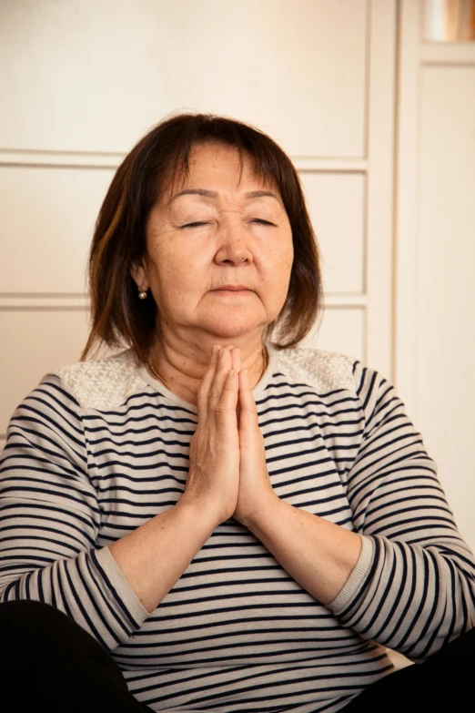 a woman sitting in a chair with her eyes closed, inspired by Hanabusa Itchō, praying posture, neck wrinkles, trending photo, russian and japanese mix