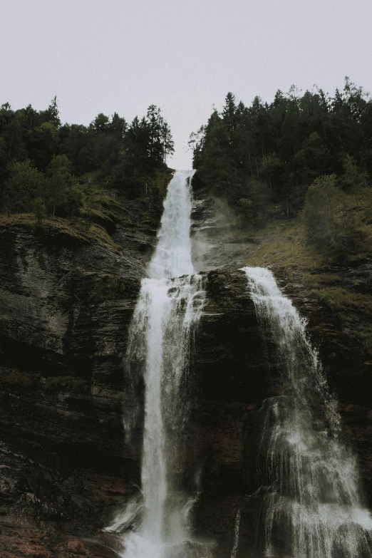 a man standing in front of a waterfall, an album cover, by Johannes Voss, unsplash contest winner, 2 5 6 x 2 5 6 pixels, trees and cliffs, shot from a distance, whale fall