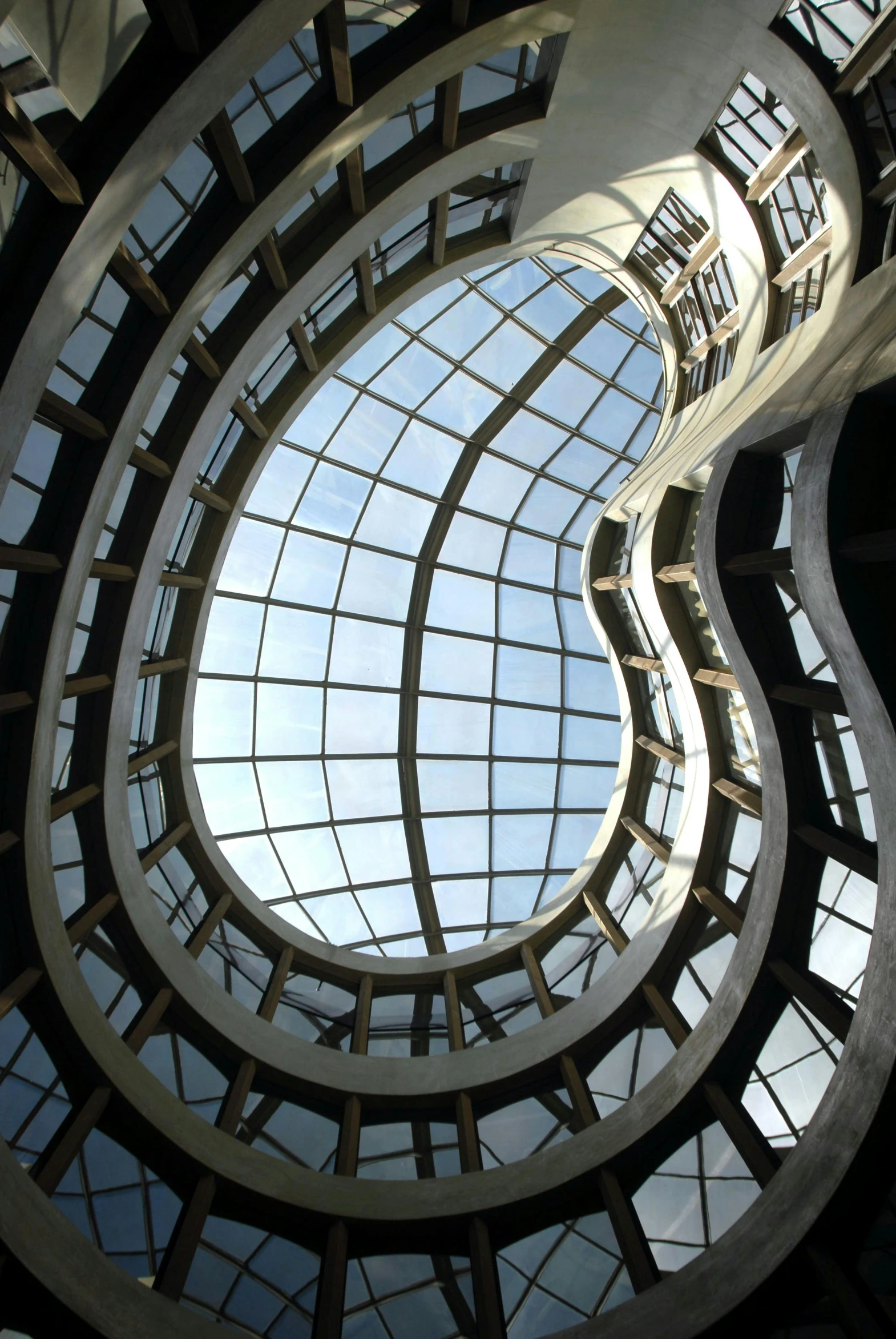 a spiral staircase in a building with lots of windows, inspired by Zaha Hadid, looking up into the sky, organic buildings, rounded roof, looking across the shoulder