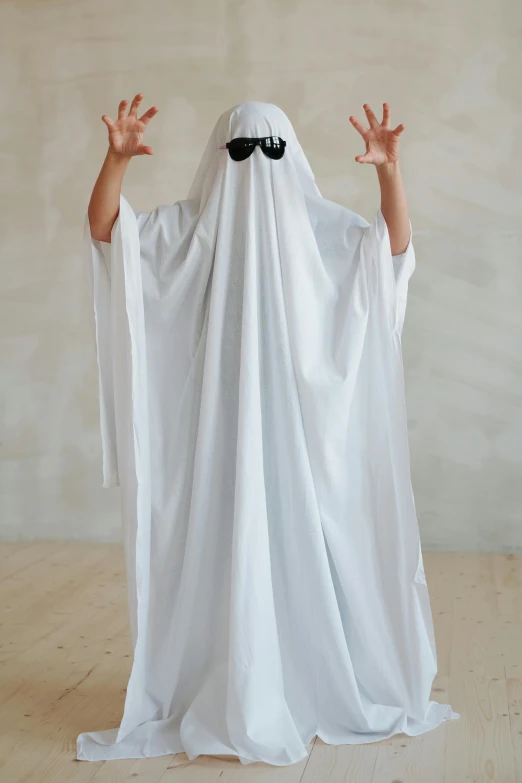 a person in a ghost costume standing in front of a wall, trending on pexels, white cloth, with arms up, costume desig, robe