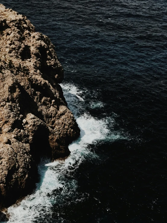 a large rock in the middle of a body of water, pexels contest winner, coastal cliffs, high angle close up shot, high contrast of light and dark, ((rocks))