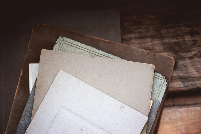 a pile of papers sitting on top of a wooden table, an album cover, inspired by Rachel Whiteread, unsplash, private press, “early 1900s daguerreotype, fine texture detail, square shapes, holding books
